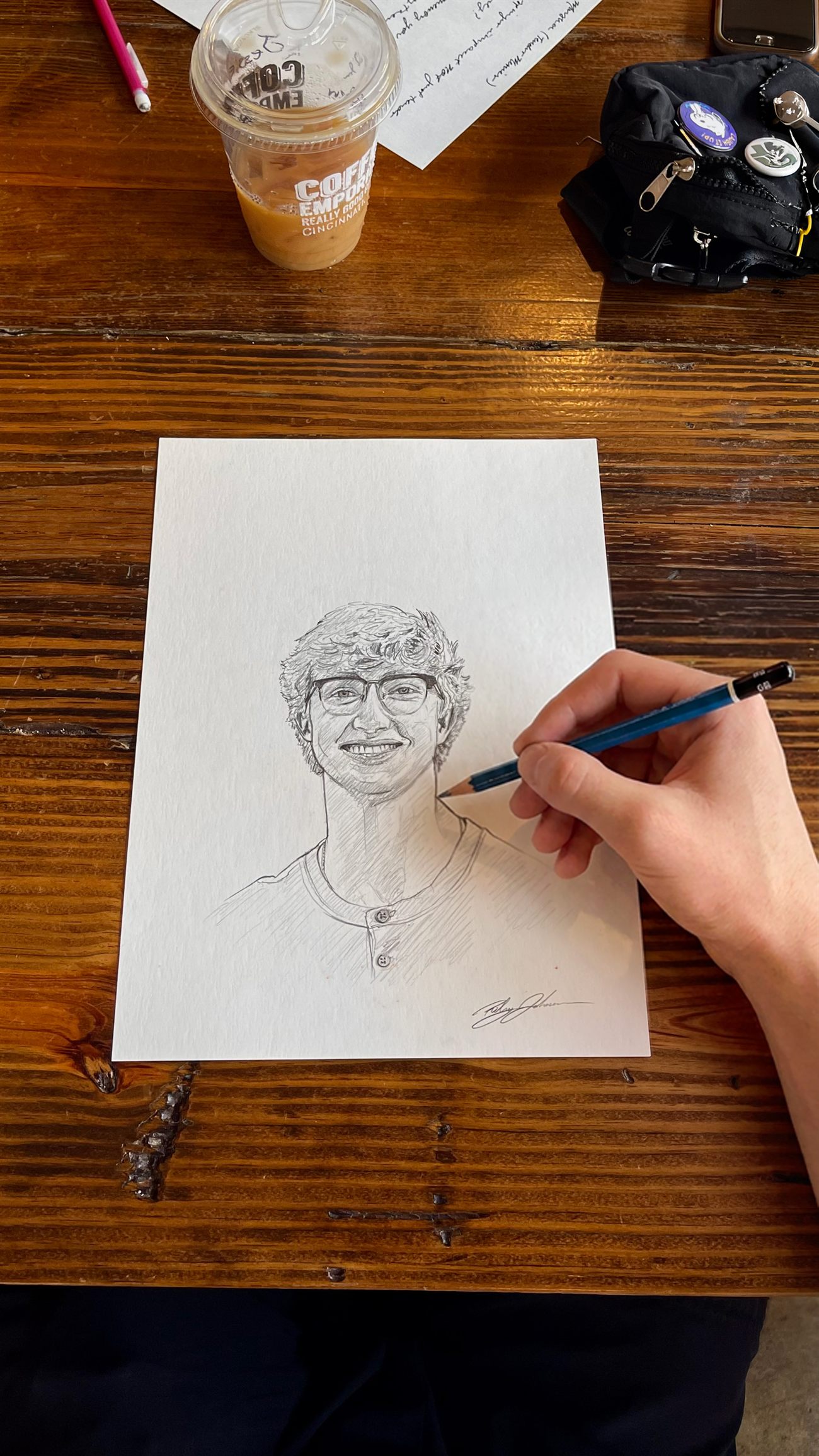 A hand drawing a detailed pencil portrait at a wooden table