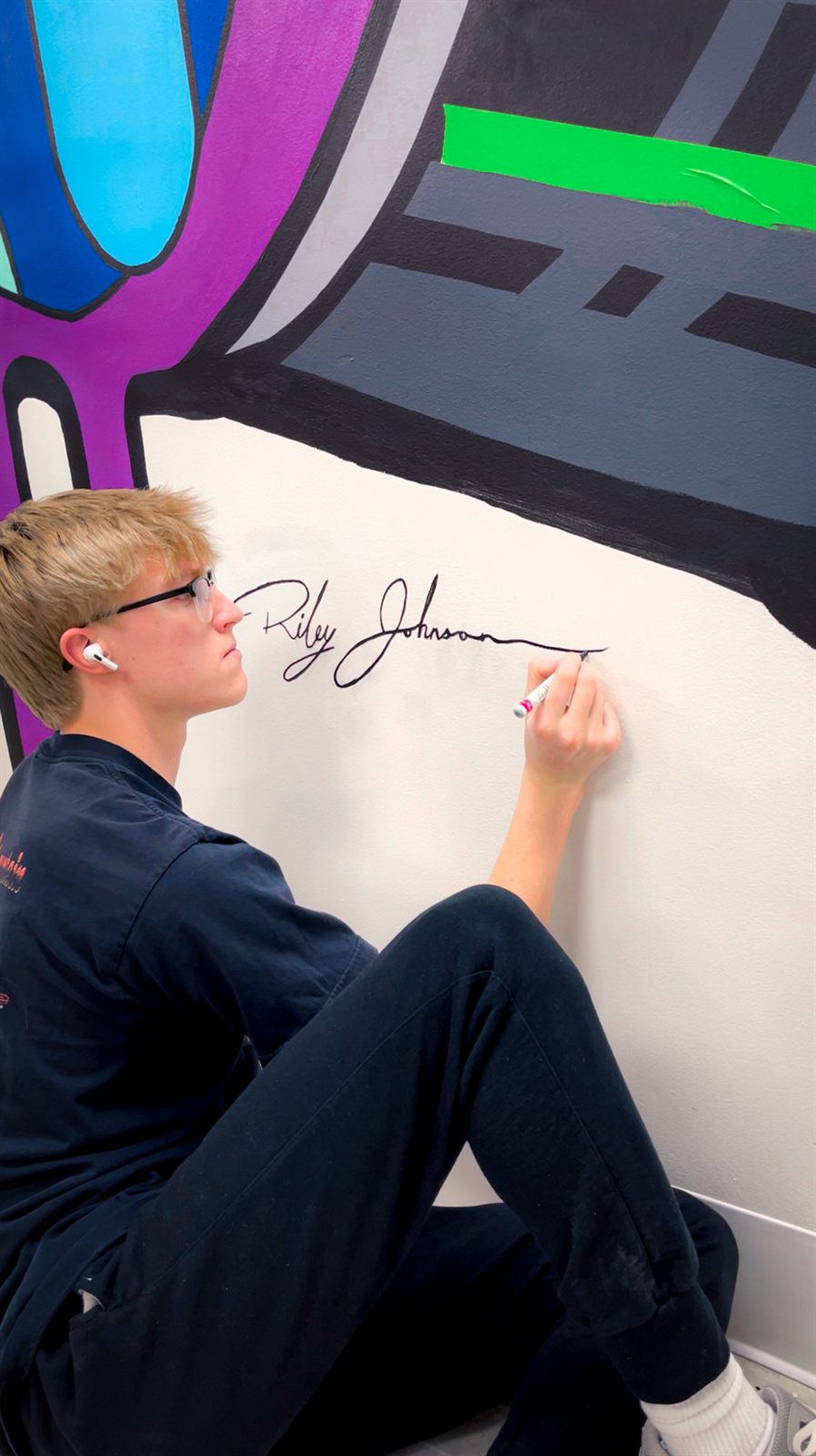 Riley Johnson signing the finished mural in black paint