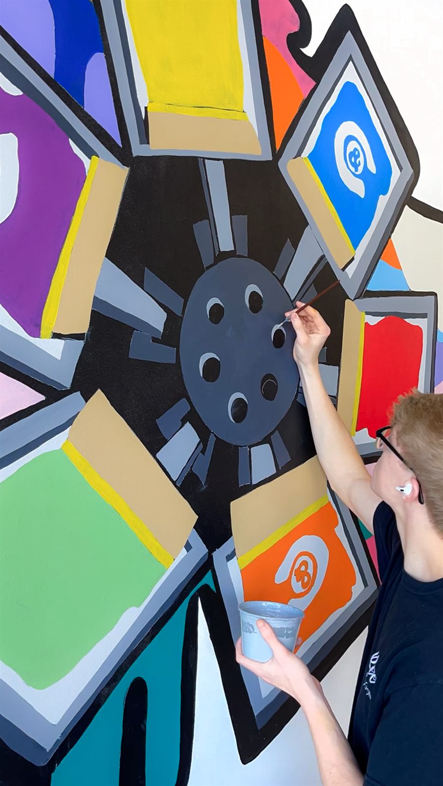 Riley Johnson painting gray keyline details on the carousel press at the heart of the mural