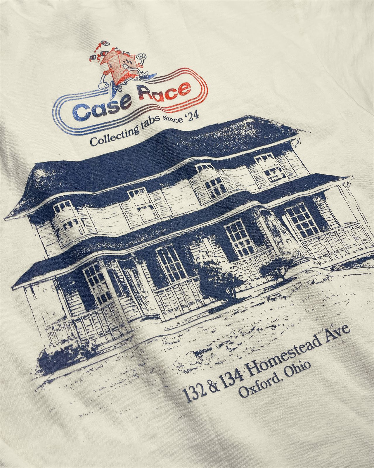 Close-up of the cream tee back print, the racetrack logo and sprinting case mascot above a navy sketch of the house