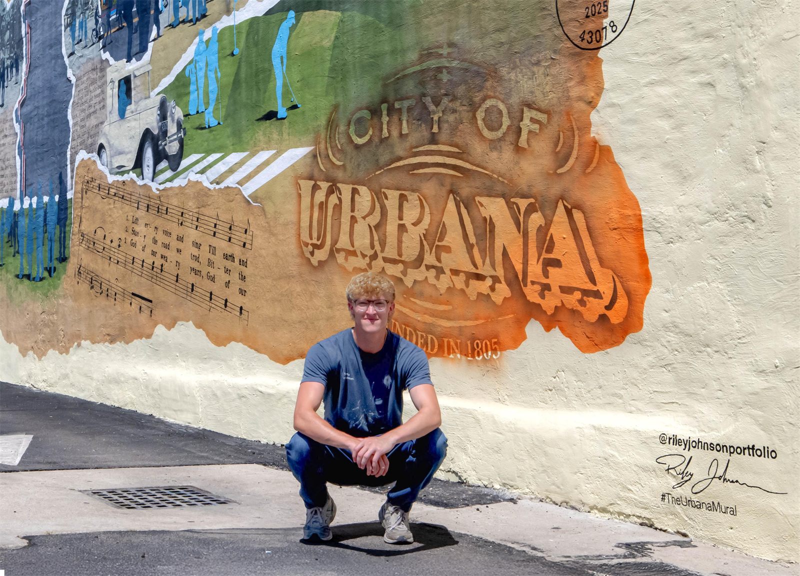 Riley Johnson crouched in front of the mural's painted City of Urbana stamp