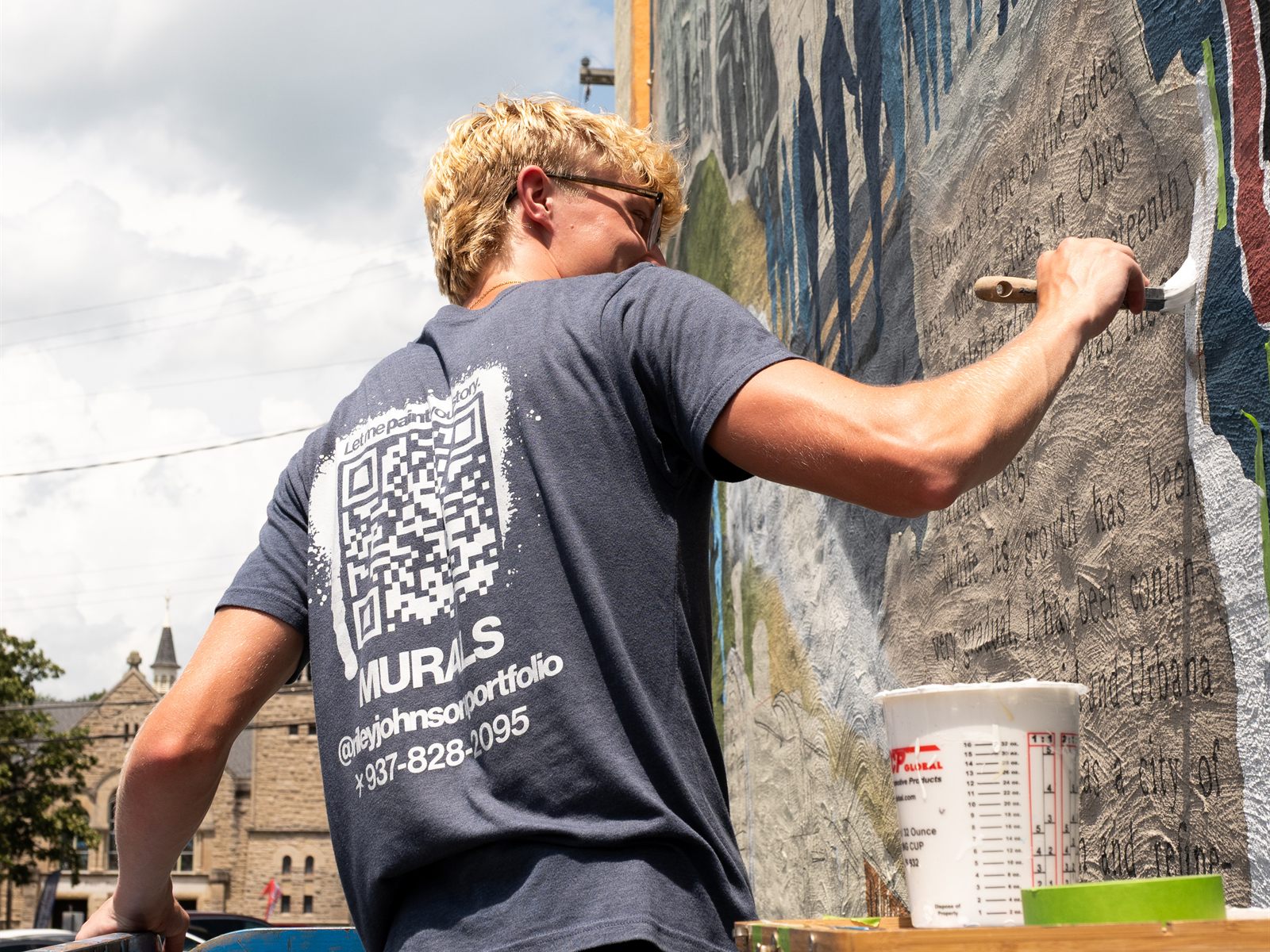 Riley Johnson brushing paint onto the mural's hand-lettered history panel while working from a lift