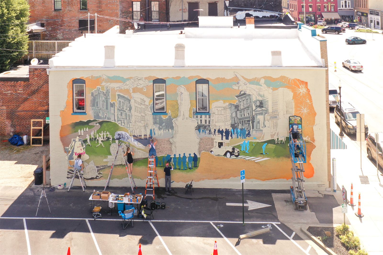 Aerial view of the mural in progress, with painters working from ladders and a scissor lift